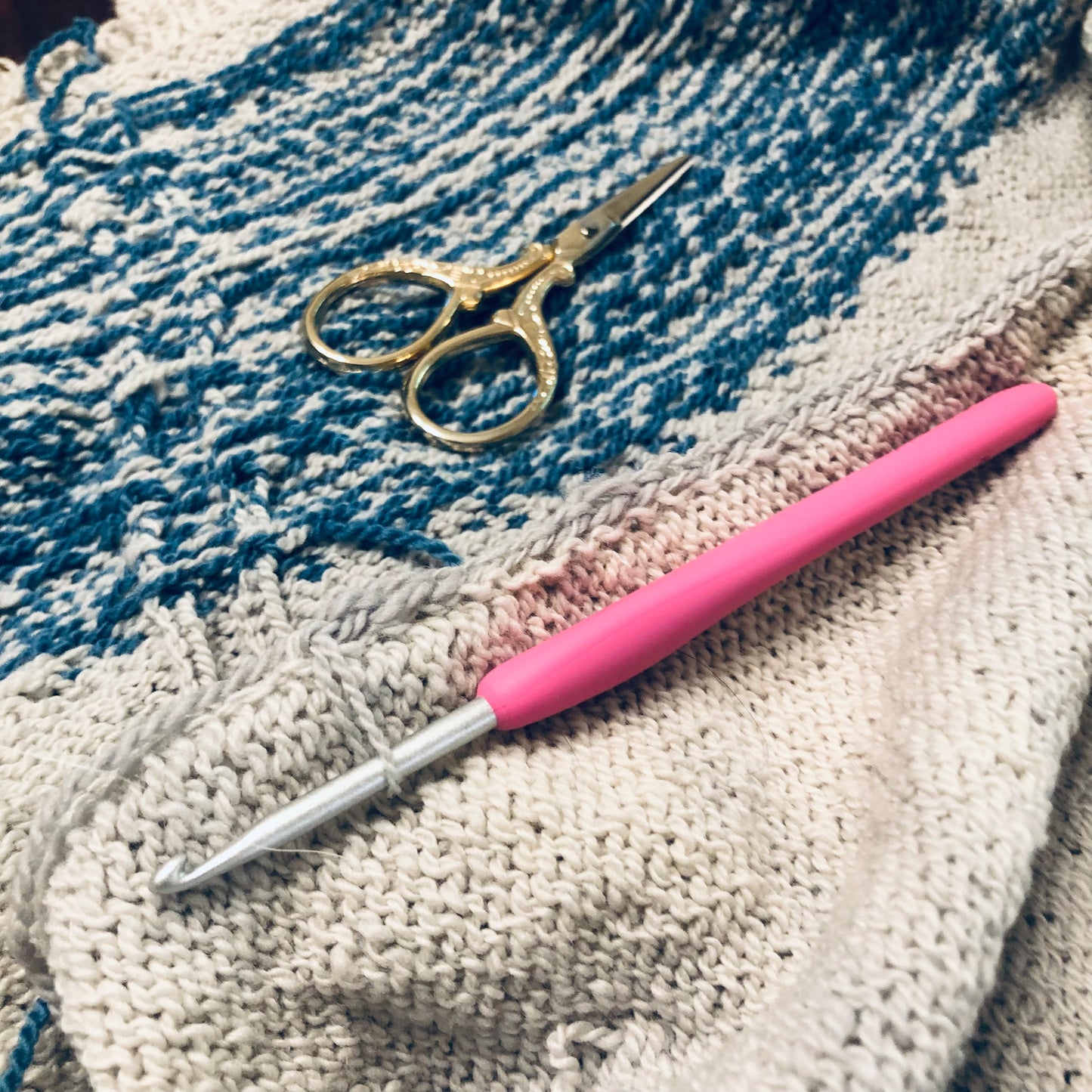 Pink crochet hook and gold scissors on a textured fabric background